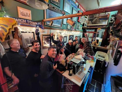 A lively group of people smiling and posing together in a cozy, decorated bar filled with memorabilia.