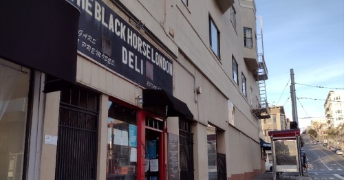 Exterior of The Black Horse London Deli, featuring a sign and a view of the street in a city setting.