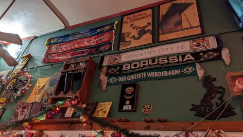 A wall decorated with various football scarves, memorabilia, and festive lights in a cozy setting.