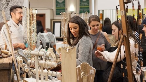 A group of women browse jewelry at a market, while a man assists them in the background.