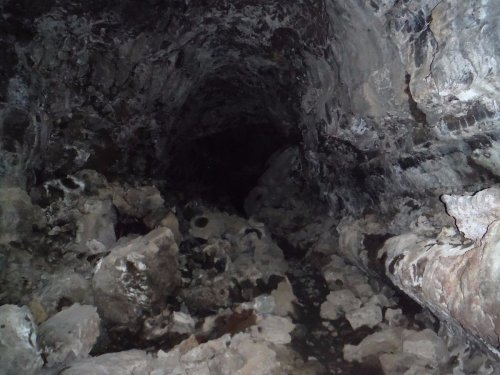 A dark cave interior with rocky terrain and uneven surfaces, leading into a shadowy passageway.