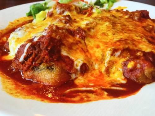 A close-up of a cheesy, saucy dish topped with red sauce, served with a side of fresh greens.