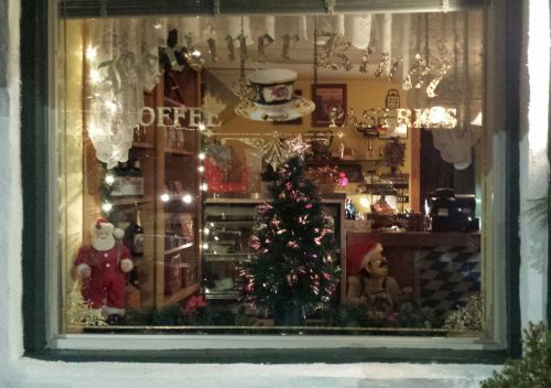A cozy café window decorated for the holidays, featuring a small Christmas tree, lights, and festive figures.