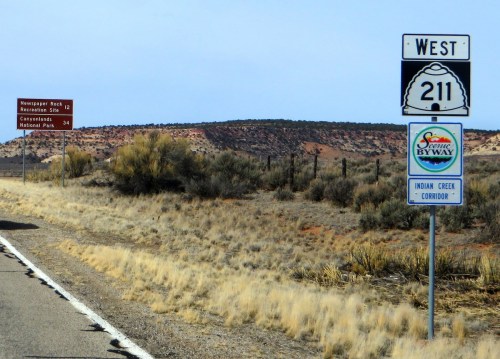 Road signs indicating West 211, Newspaper Rock Recreation Site, and Canyonlands National Park, with desert landscape.
