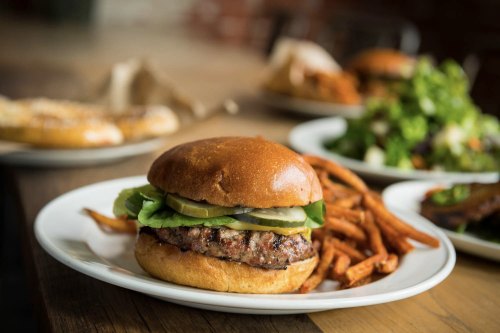 A juicy burger with pickles and lettuce, served with sweet potato fries on a white plate.