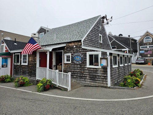 A quaint seafood restaurant, Lobster Shack, with a shingled exterior, American flag, and flower planters on a foggy day.