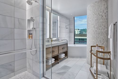 Modern bathroom featuring a glass shower, freestanding tub, and elegant marble tiles. Natural light from a window.