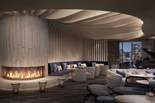 Modern lounge with a curved fireplace, plush seating, and elegant decor, featuring city views through large windows.