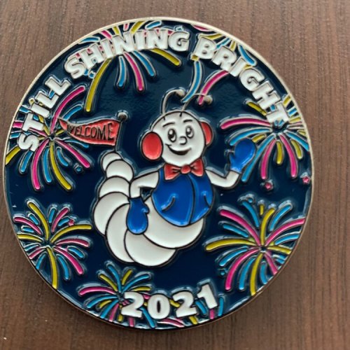 A colorful medal featuring a cartoon worm with fireworks and the text "Still Shining Bright 2021" and "Welcome."