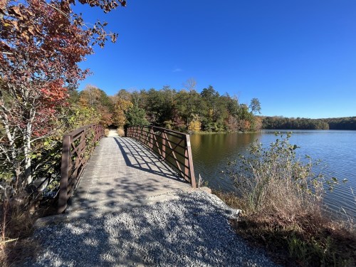 A wooden bridge over a calm lake, surrounded by colorful autumn foliage and clear blue skies.