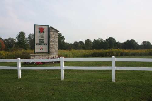 Sign for Sandy Ridge Reservation surrounded by green grass and trees, with a white fence in the foreground.