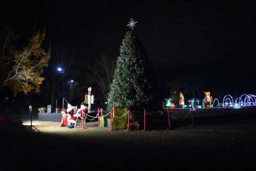 A decorated Christmas tree and Santa Claus display illuminated at night, surrounded by festive lights in a park.