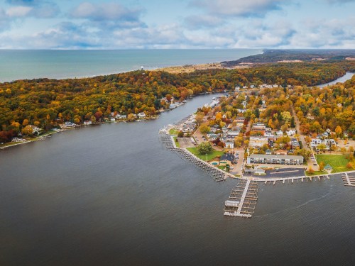 Aerial view of a coastal town with autumn foliage, a winding river, and docks along the shoreline.