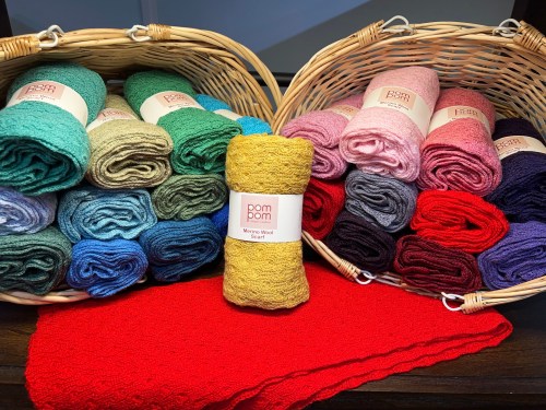 Two baskets filled with colorful yarn rolls, with a golden yarn skein in front and a red fabric piece below.