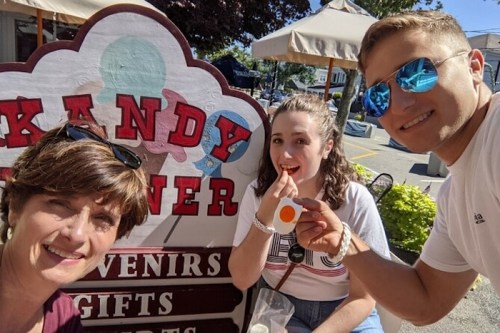 Three people smiling in front of a colorful "Kandy Corner" sign, enjoying treats on a sunny day.
