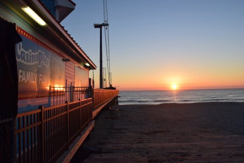 Sunset over the ocean with a boardwalk and a colorful building in the foreground.