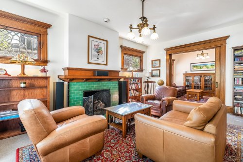 Cozy living room with leather chairs, a green-tiled fireplace, and wooden bookshelves, featuring warm lighting and decor.