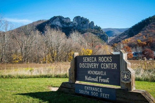 Sign for Seneca Rocks Discovery Center in Monongahela National Forest, with rocky mountains and autumn foliage in the background.