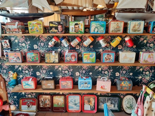 A colorful display of vintage lunchboxes arranged on shelves against a floral wallpaper background.