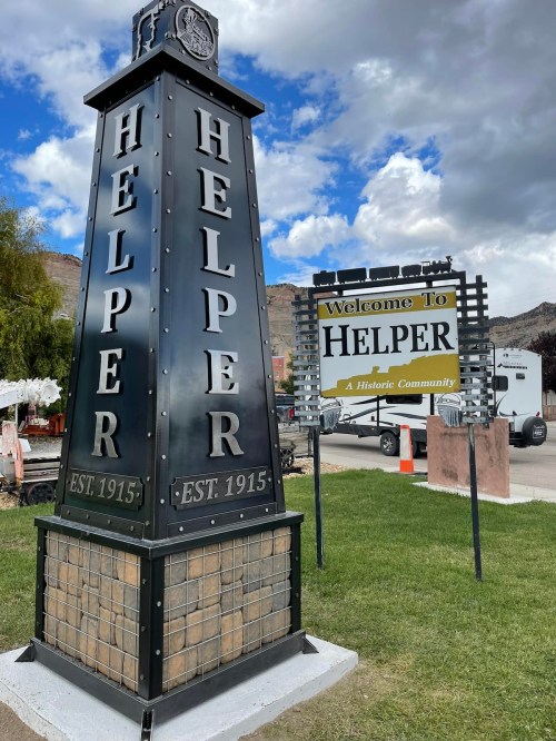 Welcome sign for Helper, a historic community, featuring a tall monument with the town's name and establishment year.