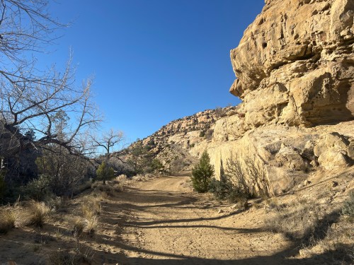 A dirt path winds through a rocky landscape with sparse vegetation under a clear blue sky.