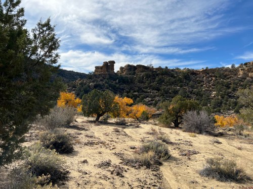A scenic landscape featuring rocky formations, autumn trees, and a clear blue sky with scattered clouds.