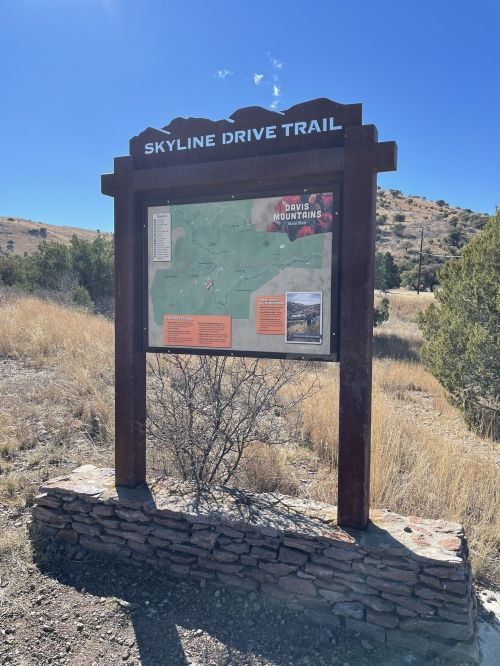 Sign for Skyline Drive Trail with a map and information about the Davis Mountains, set against a clear blue sky.