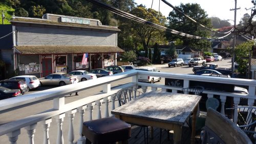 A view from a balcony overlooking a street lined with parked cars and a small store with an American flag.