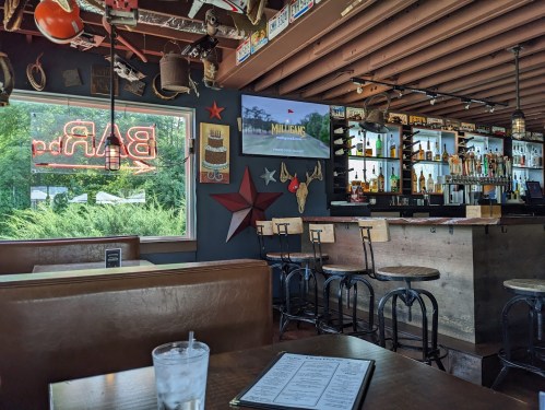 Interior of a bar with a view of the outside, featuring a TV, shelves of liquor, and a menu on the table.