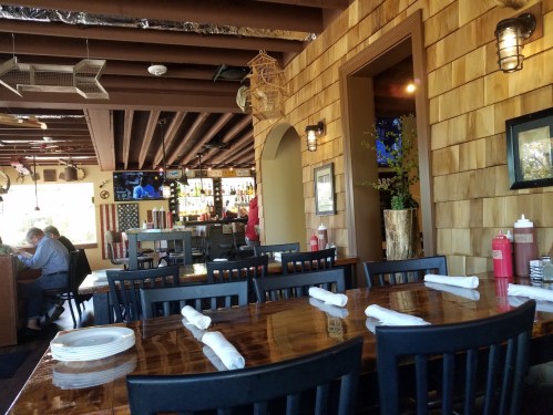 Interior of a restaurant featuring wooden decor, a bar area, and a dining table set with plates and napkins.