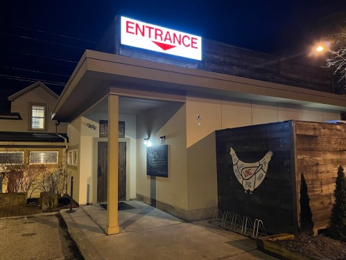 A well-lit restaurant entrance at night, featuring a prominent "ENTRANCE" sign and a wooden structure nearby.