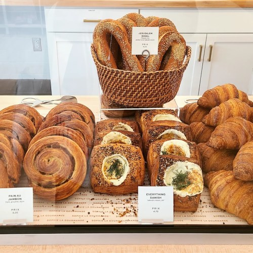 A display case filled with various pastries, including croissants, danishes, and bagels, labeled with prices.