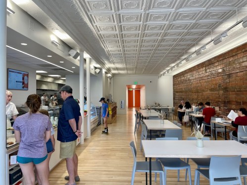 A modern café interior with a long counter, customers ordering, and tables occupied by diners in a bright, airy space.