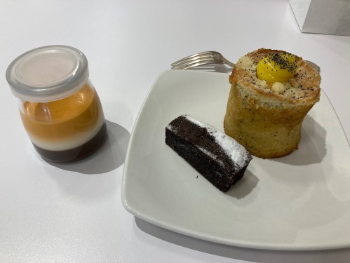 A plate with a layered dessert in a jar, a chocolate brownie, and a round cake topped with a yellow glaze.