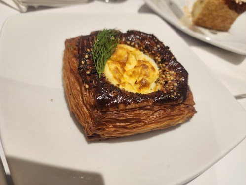A flaky pastry topped with a creamy filling and herbs, served on a white plate.