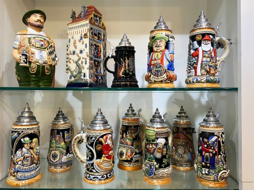 A display of decorative beer steins featuring intricate designs and characters, arranged on a glass shelf.