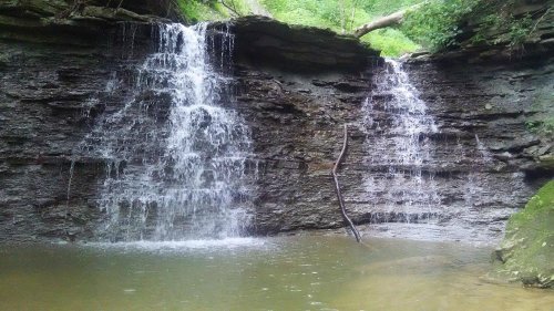 A serene waterfall cascading over rocky cliffs into a calm pool, surrounded by lush greenery.
