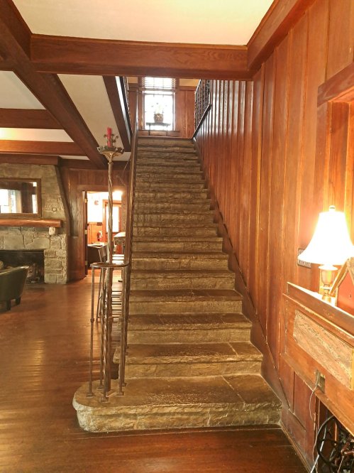 A wooden staircase leads to an upper level, surrounded by rich wood paneling and a cozy living area.