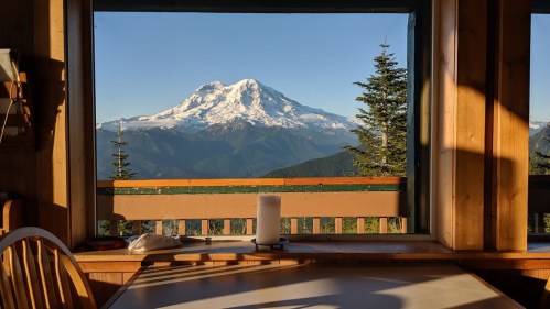 A stunning view of a snow-capped mountain through a wooden window, with a table and candle in the foreground.