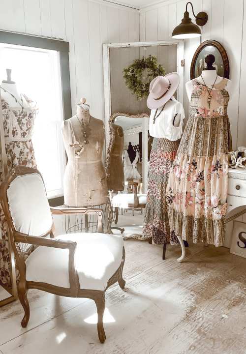 A vintage-inspired boutique with floral dresses, a mannequin, and a stylish chair in a bright, cozy setting.