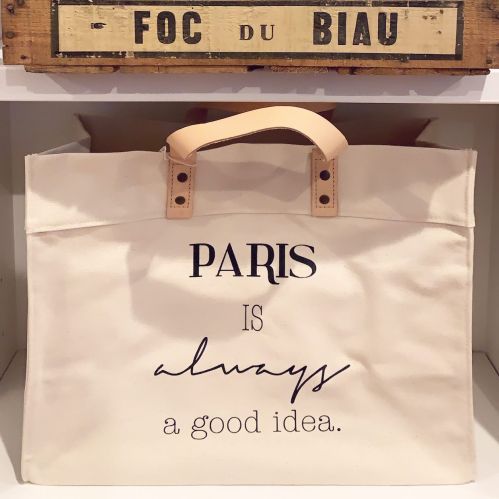 A cream tote bag with the text "PARIS is always a good idea" printed in stylish fonts.