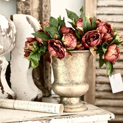 A vintage vase filled with red and orange flowers, set against a rustic background with wooden textures.