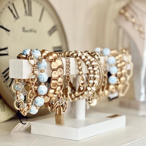 A display of gold and blue bracelets on a white stand, with a vintage clock in the background.