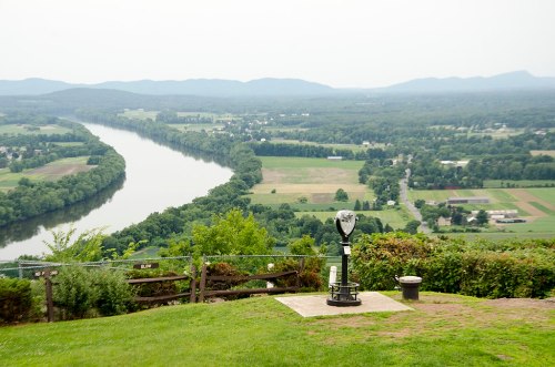 A scenic view of a river winding through green fields, with a viewing telescope in the foreground.