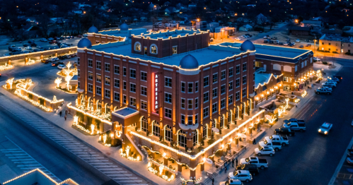 Aerial view of a beautifully lit building adorned with holiday lights, surrounded by parked cars and a festive atmosphere.