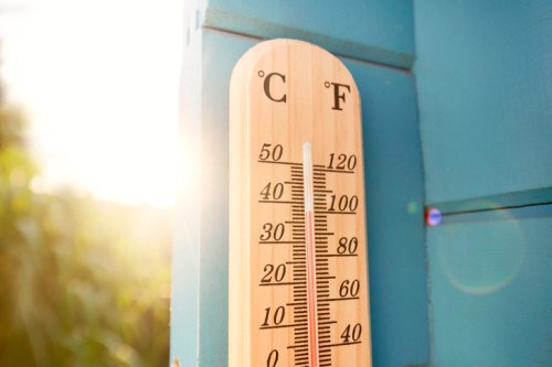 A wooden thermometer displaying Celsius and Fahrenheit temperatures, with sunlight in the background.