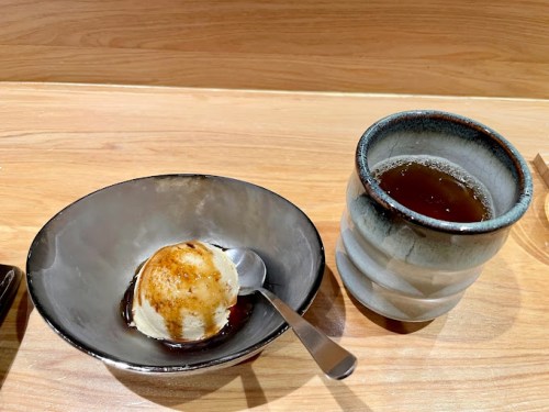 A bowl of ice cream with a caramelized top and a cup of dark tea on a wooden table.