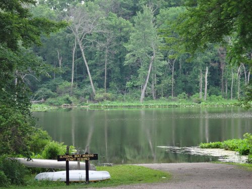 A serene lake surrounded by trees, with a sign for seasonal boat mooring in the foreground.