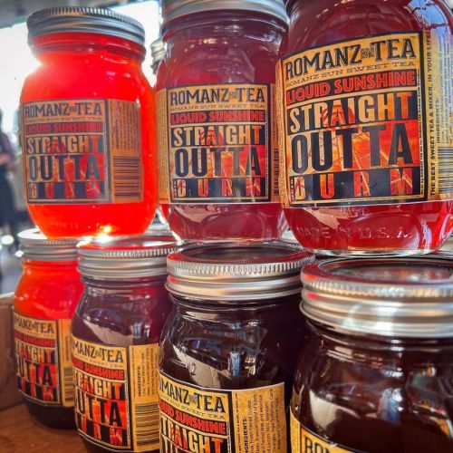 A display of colorful jars of tea labeled "Liquid Sunshine" and "Straight Outta Burn" stacked together.