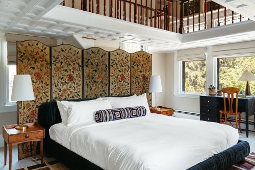 A cozy bedroom featuring a large bed, decorative screen, bedside tables, and a desk with a chair in a bright, airy space.